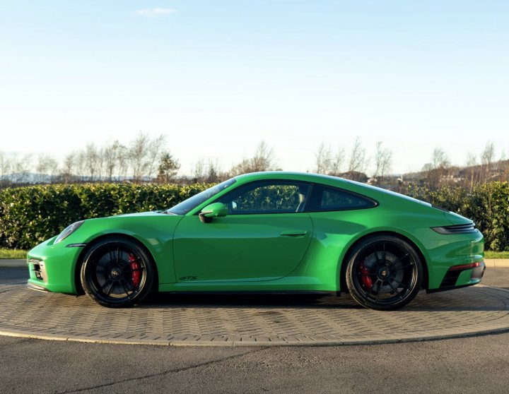 Pistonheads - The image shows a vibrant green Porsche sports car parked on a driveway. The car has a sleek design, with the hood and side mirrors painted in glossy black contrasting with its green body. It's equipped with black rims that add to its sporty appeal. Behind the vehicle, there's a serene setting with a hedge lining the driveway and trees in the background under a clear sky. The car is positioned slightly off-center, creating a dynamic composition that showcases both the car and its surroundings.