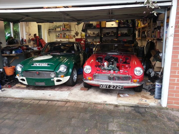 To go semi-Sebring/bumperless (MGB) or not? - Page 1 - MG - PistonHeads - The image captures a well-lit, spacious garage housing two vintage car models. A green vintage vehicle is parked next to a red one, suggesting a passionate collector's space. Various tools and equipment scattered throughout the garage indicate an active workspace for maintenance and restoration. The garage appears to be attached to a brick building, suggesting a blend of modern garage access with traditional architecture. The overall ambiance conveys a sense of nostalgia, reflecting the timeless charm of these classic cars.