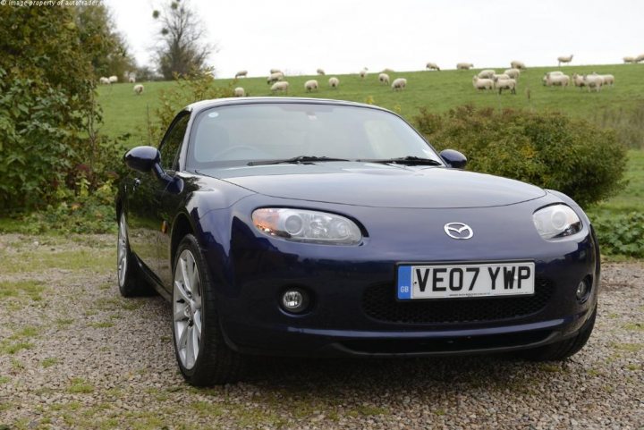 MK3 MX-5 for a 20 year old? - Page 1 - Mazda MX5/Eunos/Miata - PistonHeads - The image depicts a black sports car parked on a gravel path. The nameplate on the car indicates it's a Mazda, possibly a model from the MX-5 Miata, with a license plate that reads "VE07 YWP." In the background, a herd of sheep is grazing in a field, adding a pastoral contrast to the urban feel of the sports car. The scene suggests a peaceful countryside setting.