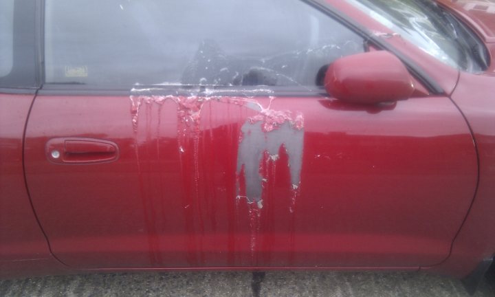 Mindless Pistonheads Vandalism Worst Mornng - This image captures a scene of a red car parked at an angle, with a notable black smear on the side panel area. The car appears to be a sedan, and there are also splatters of what seem to be ice cream or a similar substance spattered across the same area, adding to the overall visual interest of the picture. The background is blurred, drawing focus to the car and the marks on it, but suggests it might be a street or parking area.