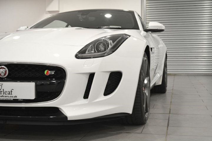 I've just bought an F-Type (pictures) - Page 1 - Jaguar - PistonHeads - The image shows a striking white Aston Martin sports car parked in an indoor space, possibly a dealership or a showroom. The car features distinctive design elements, including the pointed front end, large intakes on the hood, and a sleek bodyline that hints at its speed and performance capabilities. At the front of the vehicle, a license plate is clearly visible, suggesting that it could be on display for potential buyers or admirers. The setting has a modern, clean appearance with a concrete floor that reflects some of the car's light, adding depth to the photograph. The overall impression is that of luxury and refinement, typical of Aston Martin vehicles.