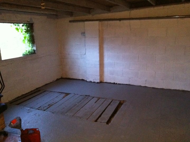 Inspection Pit Cover - Page 1 - Homes, Gardens and DIY - PistonHeads - This image captures a room that is in the process of being renovated or repaired. The walls and floor are covered in white tiles, giving the room a clean, unfinished look. A notable feature is a large, empty square in the middle of the room, which could be a demolition area or a place awaiting new construction or installation. To the left, there is a window with no curtains or blinds, allowing natural light to fill the space. On the right side of the room, a portion of a door can be seen, perhaps leading to another space or function. The room has a variety of textures, with visible elements like cables and wood panels, hinting at the ongoing work.