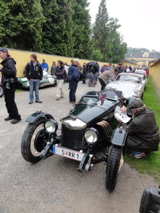 Celebrating 20 years of ... - Page 1 - Vipers - PistonHeads - The image showcases a vintage car show taking place in an outdoor setting. At the center of the scene, a man is inspecting the hood of a black vintage car. The car is adorned with a number "SERR1" and proudly displays a German license plate, suggesting its possible origin or heritage. 

Surrounding the vintage car, there are several other classic vehicles and a few painted yellow, indicating the theme or brand associated with these cars. A group of people, some of whom are holding umbrellas, are gathered around, possibly appreciating the antique cars and their history or design. 

The event seems to be well-attended, with a crowd gathered around the cars on the field, probably discussing the cars or simply enjoying their time at the show. The presence of a backpack suggests that some attendees have come prepared to spend a significant amount of time at this venue, perhaps to explore all the vintage cars on display. 

Overall, the image captures a nostalgic moment where enthusiasts gather to admire the history and craftsmanship of vintage cars.