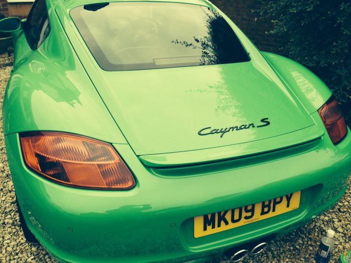 Black paint code for R spoiler, vents and mirrors - Page 1 - Boxster/Cayman - PistonHeads - The image presents a vibrant scene featuring a green sports car parked on a gravel driveway. The car, boasting a sleek design and a yellow license plate with the letters "MK09 BPY", sits majestically on a bed of gravel. In the top left corner of the image, a small plant steals the viewer's attention, adding a touch of nature to the man-made beauty of the car. Toward the top right corner, a bottle stands, perhaps holding a refreshing beverage. The image overall paints a picture of a tranquil afternoon spent in the company of a fine automobile.