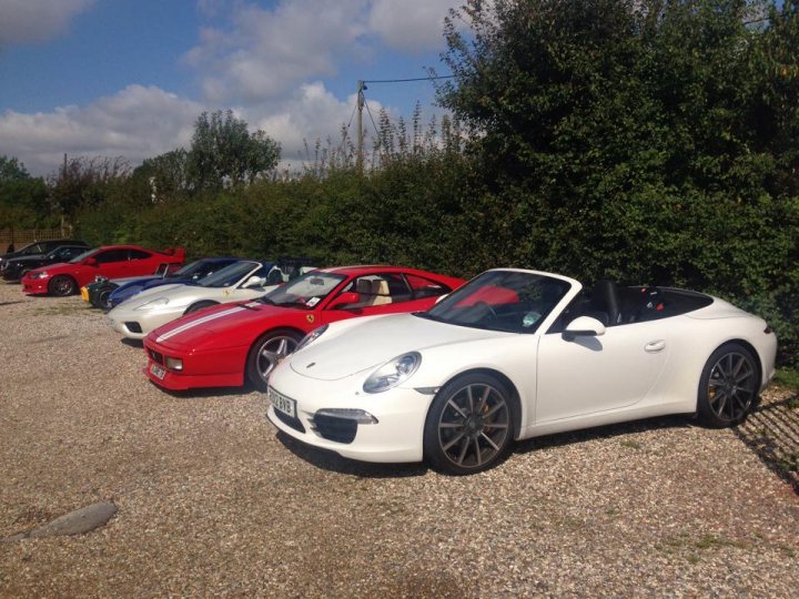 *** Essex Breakfast Saturday August 9th ******* - Page 1 - Kent & Essex - PistonHeads - The image features a row of parked sports cars situated on a gravel area. In the foreground, there's a bright white Porsche car with a tidy appearance, including a neatly tucked-in window and wheel covers. The car is positioned to the left side of the image with its nose facing the camera lens.

Behind the Porsche, a collection of other vehicles can be seen, including red and white varieties. The cars are aligned in a straight line, showcasing their sleek designs and shiny surfaces. The surroundings suggest a calm and clear day with a blue sky and some greenery visible in the background.

The arrangement, condition, and placement of the cars indicate that they are part of a collection, possibly at a special event or gathering focused on sports car appreciation. The cars are parked in a neat and organized fashion, which further highlights their treasured status to the enthusiasts who visit the site.