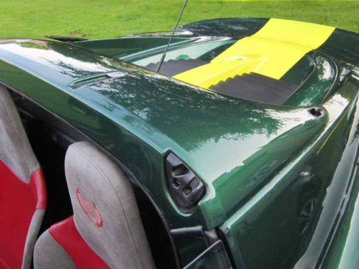 OCD - Page 1 - Elise/Exige/Europa/340R - PistonHeads - The image shows the luxurious interior of a green sports car, focusing on the rear seats that are predominantly grey with a striking red accent. There is a sunroof which is partially open, allowing a glimpse of fresh air. A yellow warning label is placed across the open space of the car seat, indicating a potential safety hazard. The interior appears to be in excellent condition, suggesting it has been well-maintained and cared for.