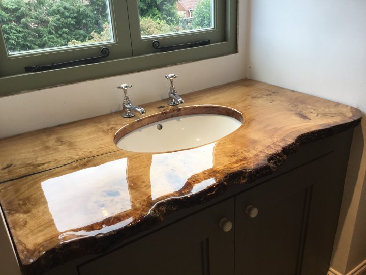 Bit of resined Oak. - Page 1 - Homes, Gardens and DIY - PistonHeads - The image presents a bathroom counter resting against a backsplash. The counter is a deep wood grain finish, giving it a polished appearance. On top of the counter sits a matching wooden sink bowl with a natural variegation of tones. The backsplash forms a smooth curve, subtly transitioning from the counter to the vertical lines, a unique design element that adds visual interest to the space. The design suggests a blend of traditional and contemporary styles, focusing on natural materials and rich textures.