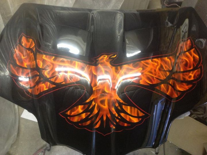 A close up of a motorcycle with a helmet on it - Pistonheads - The image showcases a black motorcycle seat with a striking fire and bird design. The emblem of a bird, outlined in red, dominates the center of the seat, conveying a sense of freedom and speed. Encircling the bird is a ring of flames, their orange and yellow hues contrasting vividly against the black seat. The flames add a dynamic element to the design, suggesting movement and intensity. The seat itself appears to be made of a glossy leather material, reflecting the image back, which further emphasizes the design.