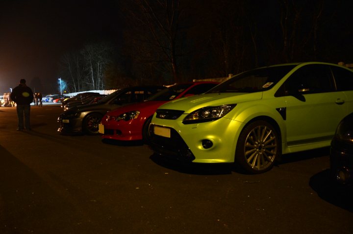 March Essex Pistonheads - The image depicts a nighttime scene in a parking lot. There are several parked cars, with the front of a green car being prominently featured in the foreground, showcasing its design with a circular emblem on the grille. Additionally, there are multiple cars in the background, some closer than others, likely indicating this parking lot is quite busy. The lighting indicates it's night, and the environment includes trees and what appear to be clear skies. The overall atmosphere of the image conveys a sense of stillness in the darkness.