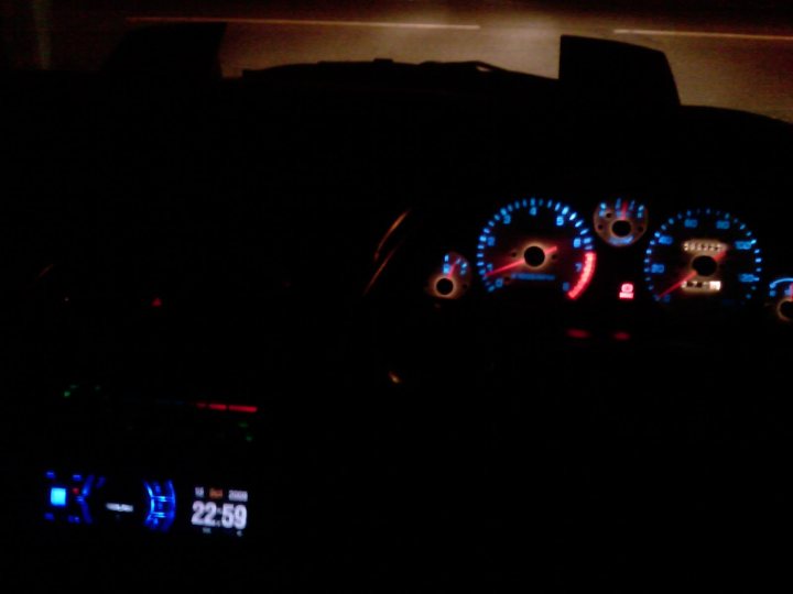 Pistonheads - The image depicts the dashboard of a vehicle at night. The main focus is the digital display showing "23:59", suggesting it's about 11:30 pm. The dashboard is equipped with various controls and indicators. Five red lights under the speedometer are illuminated, which typically stand for error codes or warnings. The overall ambience of the image conveys a quiet atmosphere inside the vehicle.