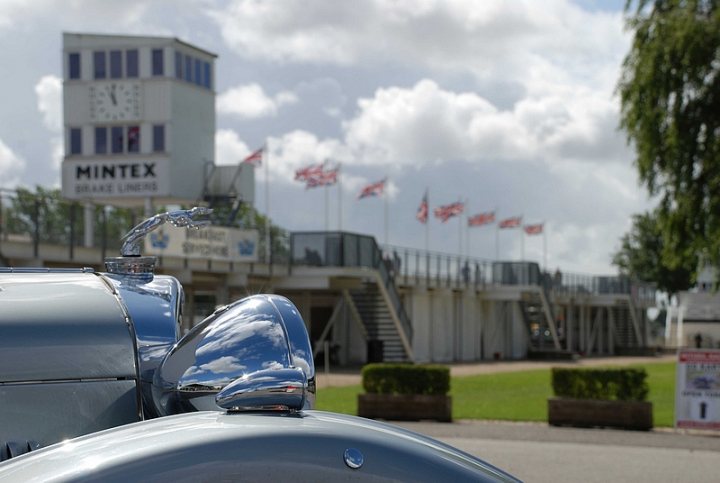 Goodwood Breakfast Club, Pre 1966 classic sunday - Page 1 - Goodwood Events - PistonHeads - The image features a vintage car from the 1950s, specifically a MG car. The car, which is the main subject of the photo, is parked in front of a building with a clock tower. Several British flags are visible, contributing to the theme of the photo. The car's side mirror and shiny body are reflecting the clear day. The setting seems to be surrounded by lush greenery, indicating a well-maintained outdoor area.