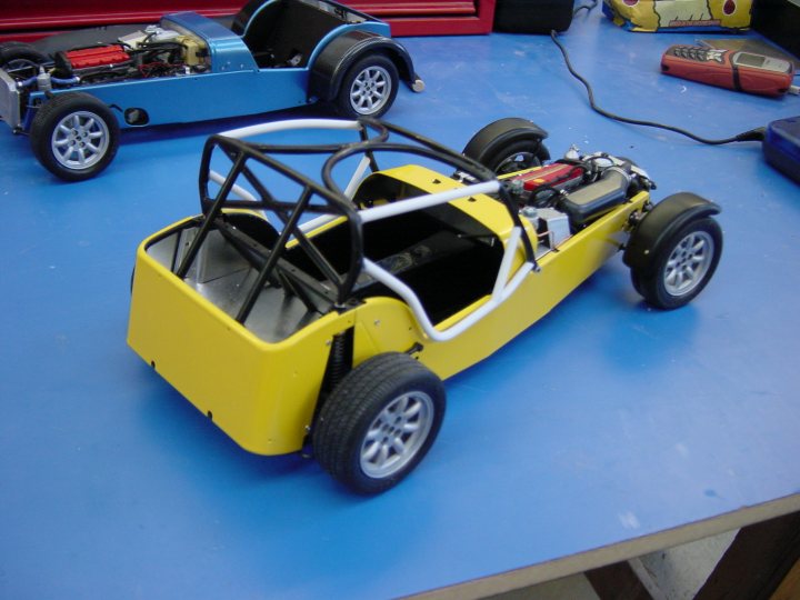 Tamiya Caterham 1/12 - modified - Page 1 - Scale Models - PistonHeads - In the image, a vibrant model car in a striking yellow hue with a contrasting black roof holds the viewer's attention. This toy car is not just any ordinary model, but it appears to be a detailed, kit-style car that is meticulously displayed. It's parked on a red baseboard, suggesting a mode of storage. In the background, partially obscured by the yellow model car, there's another car, possibly another model or color variant. The scene seems to be arranged to showcase the intricate details of the yellow car, indicating a pride in its craftsmanship.