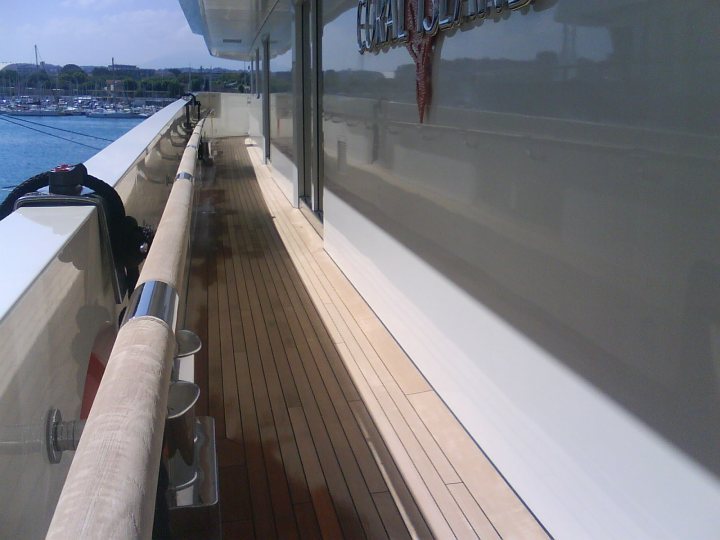 Million Yachts Super Pistonheads - The image shows the deck of a boat, with tables and chairs. There's a view overlooking what appear to be multiple boats docked nearby. The deck itself has a dark railing, and on the side, there's text that's partially obscured. The lighting suggests it's daytime, and the overall scene gives the impression of a calm day at sea.