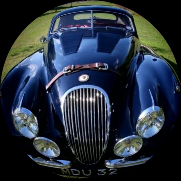 Coupe Pistonheads Fixed Head - The image features a classic blue car, possibly a vintage model, with chrome accents. The car's hood is open, revealing its engine. It is parked on green grass, and the background is either blurred or less bright, making it difficult to discern. The most striking detail in the image is the blurred circular pattern in which the car is centered, which creates a vignette effect that draws attention to the vehicle.