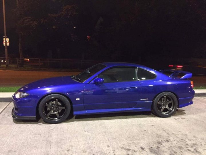 2002 Nissan Silvia Spec R (S15) - Page 1 - Readers' Cars - PistonHeads - In the calm of the night, a vibrant blue sports car rests on the asphalt. The vehicle, adorned with black trim, is stationed on a patch of grass adjacent to the parking lot. The rich hue of the car contrasts with the sepia tone of the night, emphasizing its presence. In the distance, the lights of an unseen object cast a warm glow on the scene, adding a layer of depth to the nighttime tableau.