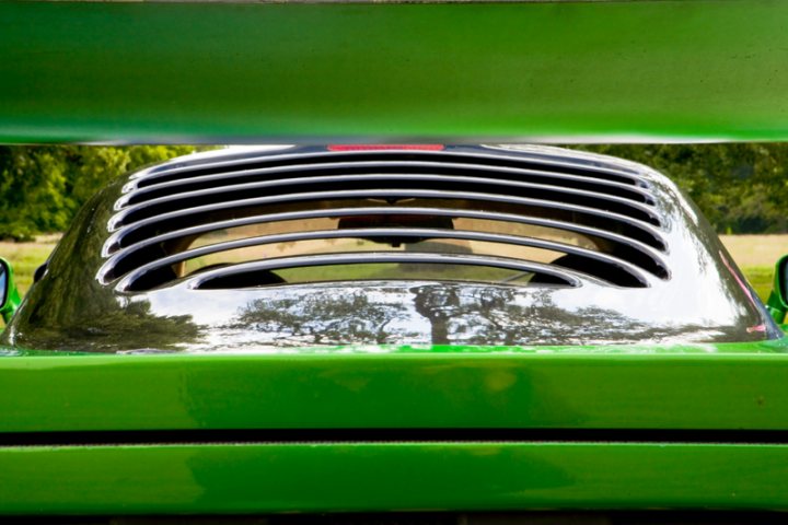 Motors Pistonheads Manor - In the image, a rear view mirror from a vehicle is captured. The mirror is reflecting the image of a lush green field behind it. The mirror itself has a black frame, contrasting with the green of the field. The rearview mirror has six blades, arranged neatly around a black center. The bottom of the image places a ramp pointing upwards, suggesting that the image may have been taken from below, possibly right under the car.