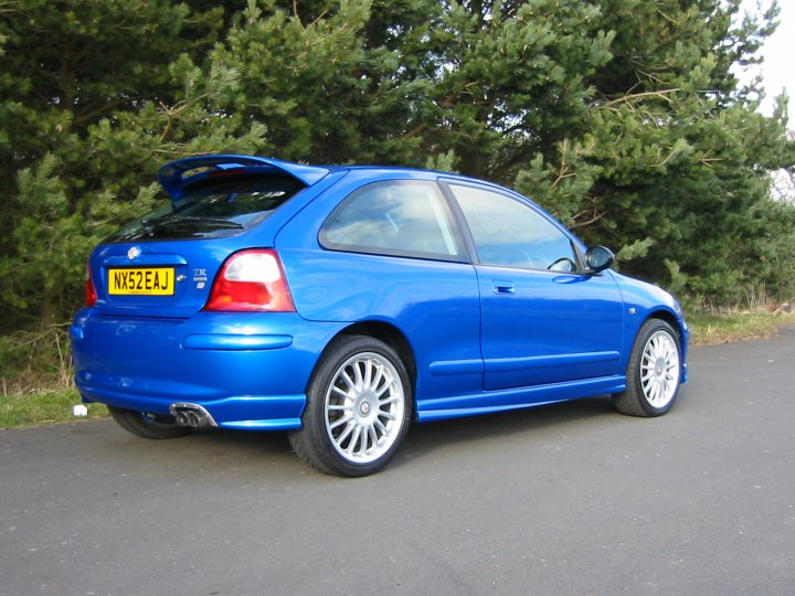 First car(s)- MG ZR - Page 1 - Readers' Cars - PistonHeads - The image shows a parked blue Toyota Celica car on a paved road. The car is currently not in use, as indicated by the license plate, which reads "DWBXE," and it is an older model, recognizable by its design and color shade. The vehicle is positioned parallel to the curb, and it is situated near some trees, suggesting the photo was taken in a residential area or park. The overall atmosphere appears calm and quiet, with no people or other moving vehicles visible in the picture.