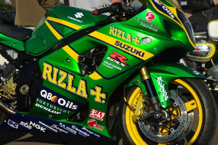 Pistonheads - The image features a vibrant green Suzuki motorcycle parked outdoors. The motorcycle is adorned with various logos and advertisements including 'OILIFE', 'R17', 'R6', 'Comfort', and 'Durthright', indicating it may be a racing motorcycle. The front wheel of the motorcycle is turned slightly to the left. The background reveals the presence of other motorcycles parked in an open space, suggesting a possible motorcycle meet or event.