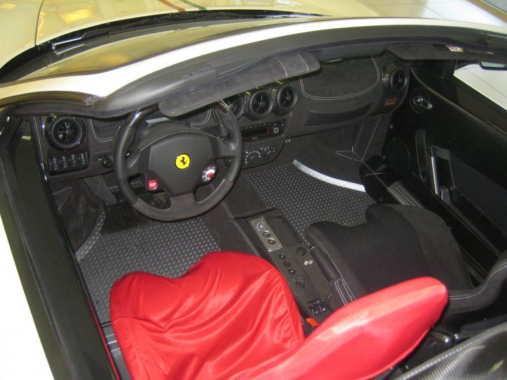 Interest Pistonheads - The image shows the interior of a vehicle, focusing on the driver's seat. This is a close-up view centered around the steering wheel, which is black with the distinct yellow Ferrari emblem. The car appears to be a luxury sedan, given the high-quality materials and craftsmanship visible in the driver's area.

On the seat in the driver's position, there's a large, red protective mat thrown over it. The upholstery in the vehicle is upgraded to red leather, luxuriously appearing soft and nice. In the center console, there is a large key or remote inside the activation mechanism, likely used to unlock or start the vehicle. The overall impression is that of a well-maintained, high-end vehicle with a focus on comfort and aesthetics.