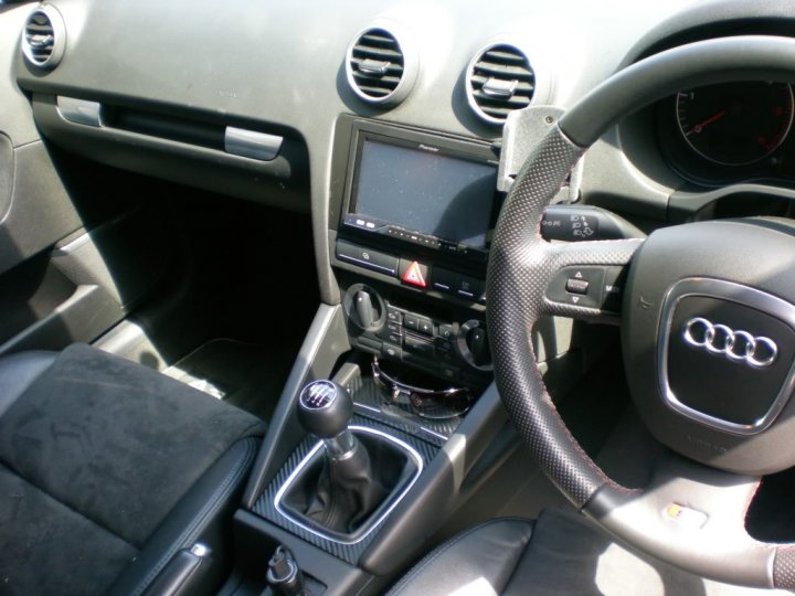 RE: Mercedes-AMG C63: Driven - Page 2 - General Gassing - PistonHeads - The image shows the interior of a metallic gray Volkswagen Cabriolet. The vehicle has a sleek design with black and silver accents. The dashboard features a black trim and houses a small LCD screen located near the center console, which is equipped with various buttons and controls. The passenger side focuses on the gear shift lever installed on the console. The steering wheel is also visible, featuring the iconic Audi emblem and multiple buttons. The seat is shown in the foreground, and the overall interior is neatly arranged with all relevant parts in order. The sunlight from the window provides a bright and clear atmosphere inside the vehicle.