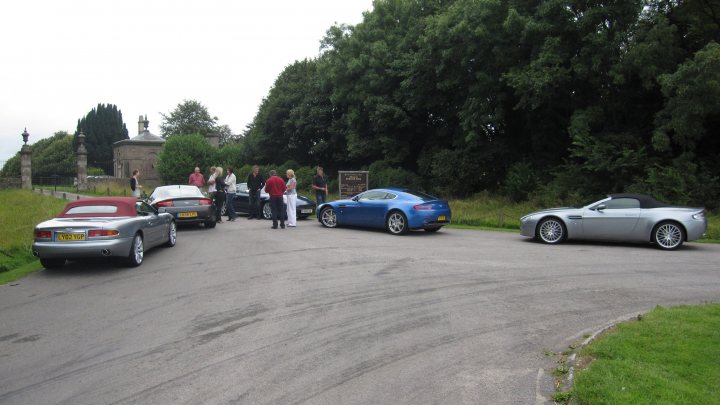 Pistonheads - The image shows a group of children standing in the middle of a road. There are various cars parked on the sides of the road. Houses and lush green trees fill the background, suggesting a residential area. The majority of the children appear to be boys, and they are dressed casually. The road on which they stand is tarred and has a gentle slope.