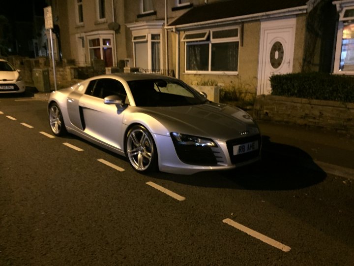 Spotted In South Wales (Vol 3) - Page 213 - South Wales - PistonHeads - The image depicts a silver Audi sports car parked on a residential street at night. The car prominently displays the Audi logo on its grille and is positioned against the curb of the street. Street markings are visible, suggesting a one-way residential area. In the vicinity, there are residential houses and streetlights provide illumination, creating a shadow of the car on the asphalt. The overall atmosphere is quiet and subdued, characteristic of a peaceful residential setting during nighttime.