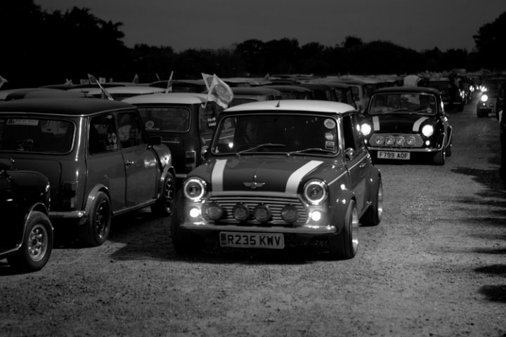 London to Brighton  - Page 1 - Classic Minis - PistonHeads - In the evocative luminescence of a night scene, the road is lined with a variety of classic cars, each with distinct features from eras past. The vehicles, bathed in spotlights, create a lap of color against the dark road.