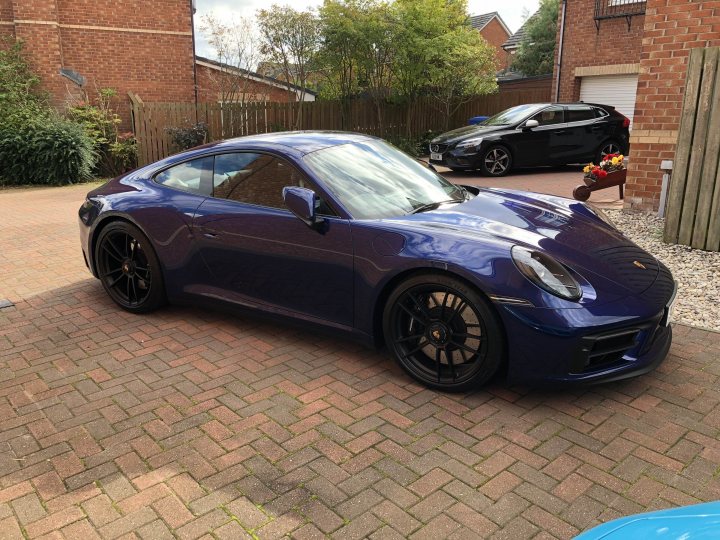 Pistonheads - The image shows a luxurious purple sports car parked on a residential street. The vehicle is sleek and polished, with a glossy finish that reflects the environment around it. It has a low-profile stance, indicating it's designed for high-performance driving. The wheels are black and appear to be alloy with a multi-spoke design. In the background, there's a residential house, suggesting a suburban setting. There are other cars parked on the street, indicating this might be a popular area or a community that appreciates automotive aesthetics.