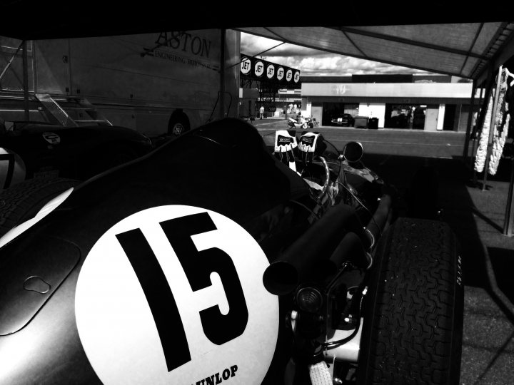 Fantastic Motorsport Photos! - Page 204 - General Motorsport - PistonHeads - The image is a black and white photograph that captures the front end of a vintage race car. The car number is prominently displayed as "15". The vehicle appears ready for a race, given its sleek design and the presence of multiple tires visible in the foreground and background. There are also numbers 15 in the background, possibly indicating a race bib or car number. Lastly, the setting seems to be a race track or garage area, with a covered area that could be a driver's pit in the background.