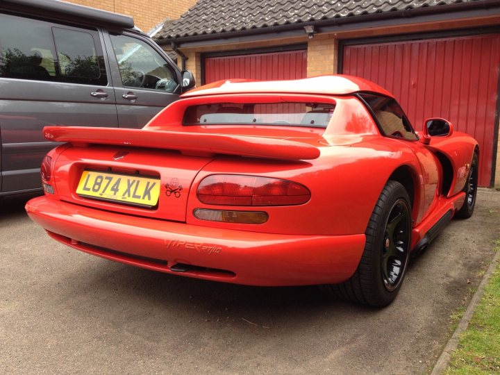 viper in bury st edmunds 17/05/2013 - Page 1 - Vipers - PistonHeads - The image features a striking red sports car parked in a driveway. The car's number plate reads "L 874 YLK", indicating its registration. The vehicle has a prominent rear spoiler, suggesting it's designed for high-speed performance. It's positioned in front of a garage door, and there's a tree visible in the background. The overall scene suggests a residential area.