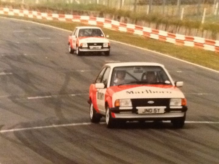 A car driving down a street next to a traffic light - Pistonheads - In the image, a dynamic scene of two Marlboro racing cars is captured on a sportscar track. The cars are moving at high speeds, their number plates clearly visible: JNOS7 on the first car and JNOS8 in the second. The track is bordered by metal fencing and orange and white safety barriers. The cars, with their distinct branding, dominate the frame, and the motion blur adds a sense of speed to the scene.