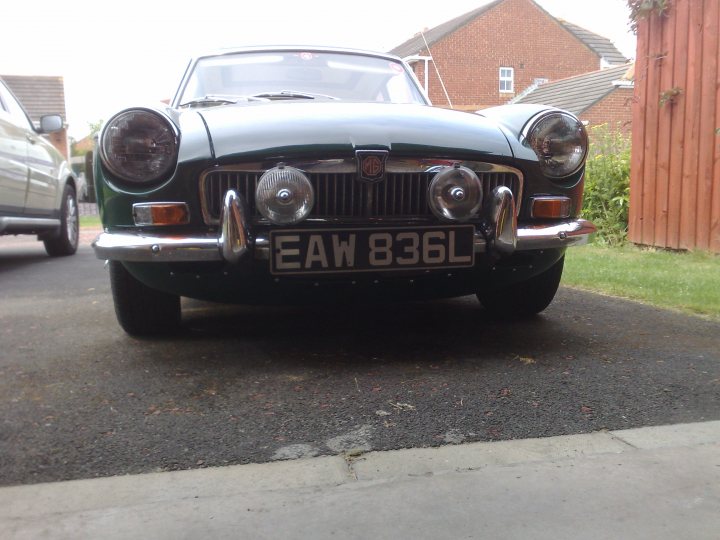 Conversion Pistonheads Sebring Mgb - The image features an old, classic car that is parked on a driveway next to a street. The car is facing towards the right side of the image and is situated in front of a house with a wooden fence and a brick facade. The car's license plate reads "E50L"} and it has two round white headlights on the front. The overall scene suggests a quiet, residential area.