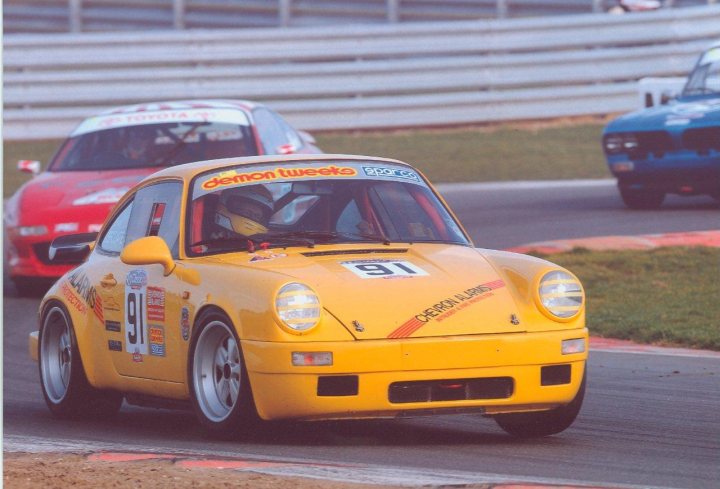 Pictures of your classic Porsches, past, present and future - Page 15 - Porsche Classics - PistonHeads - The image captures an exciting moment on a race track, where a vibrant yellow racing car is in motion. The car, adorned with various sponsors and the number 91, is navigating a sharp left turn on the track. Another car can be seen in the background, indicating that the race is in progress. A sense of speed and precision is palpable as the car leans into the turn, emphasizing the skill and concentration of the driver. This is a dynamic scene that encapsulates the thrill of car racing.