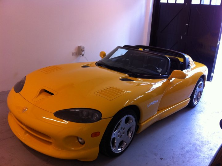 Pistonheads Wait Worth Long - The image shows a vibrant yellow sports car indoors. The car, with its sleek design and prominent air intakes, appears to be in pristine condition. It's parked close to a wall, and there are two doors visible on the right side. The interior space surrounding the vehicle is relatively simple, suggesting the focus is on the car itself. The contrast between the bright yellow of the car and the more muted colors of the indoors space makes the car stand out prominently.