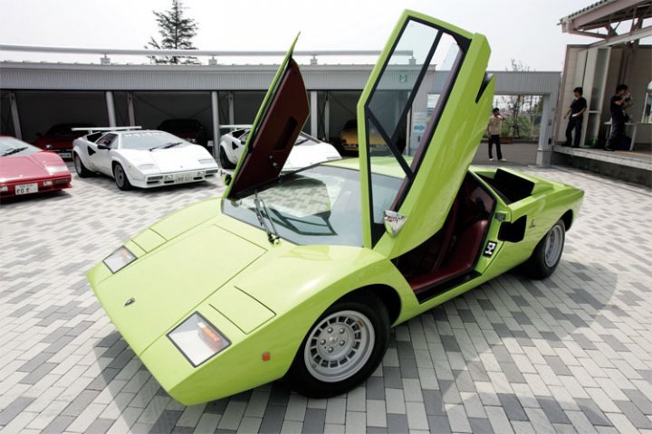 Countach  - Page 6 - Lamborghini Classics - PistonHeads - In the image, there's a striking green Lamborghini parked inside a garage with a floor made of gray and white bricks. The car's silhouette is unmistakable, with two doors on the side. Behind the Lamborghini, cars are housed in a row, each color contrasting with the vibrant green of the Lambo. Two people are standing in the background, possibly admiring the lineup of classic cars, including a red sports car in the far distance. The garage itself seems well-lit and spacious, with the brick wall adding texture and color to the setting. The overall scene suggests a passion for automobiles, particularly vintage models.