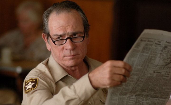 Pistonheads - In the image, the esteemed actor Gene Hackman is captured in the foreground. He's seated at a table, deeply engrossed in a newspaper. He's wearing a classic Sheriff badge, suggesting his character might be of a law enforcement background. His glasses and serious expression convey a sense of intensity and concentration. The blurred background is not explicitly explained, but it gives the impression of a public place.