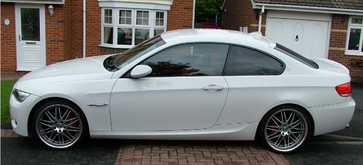 RYO" NORTH EAST TOUR 2013  RYO" - Page 1 - North East - PistonHeads - This image depicts a white BMW sports car parked on a brick driveway in front of a brick house with a white door. The car features alloy wheels and a sleek exterior design. It is daytime and the weather appears to be overcast. There is a reflection of a fir tree on the car's side window, indicating the presence of the tree in the background.