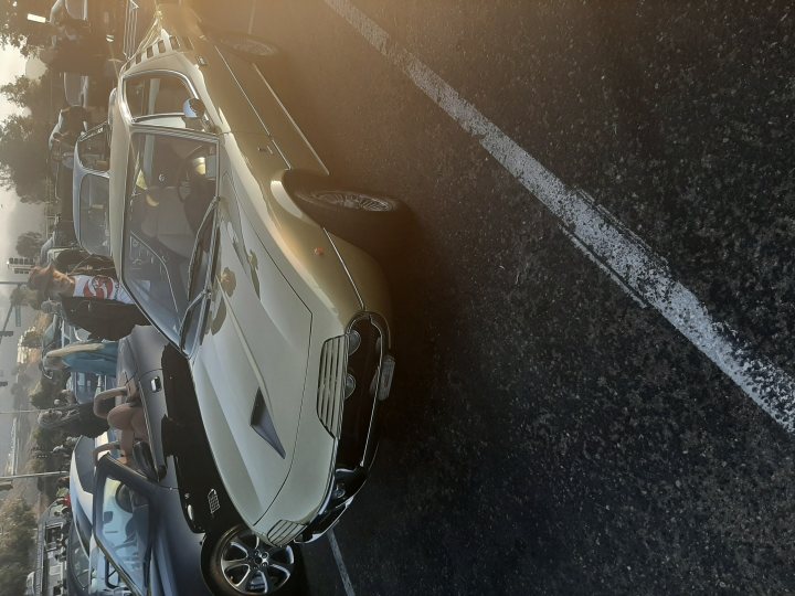 My 1972 De Tomaso Pantera - Page 3 - Readers' Cars - PistonHeads - This image showcases a vintage sports car, painted in a light beige color, parked in a parking lot during the day. The car has an open top and is adorned with various badges on its side. There are two people standing behind the vehicle, engaged in conversation. The background reveals other cars and a clear sky, suggesting a pleasant day.