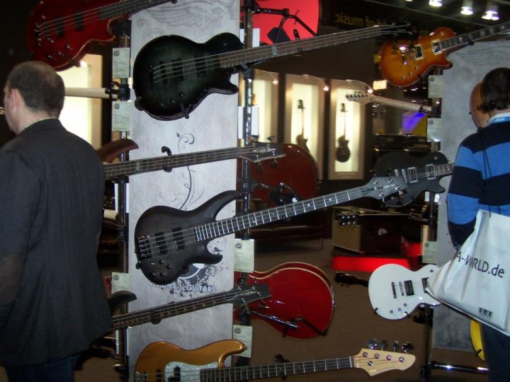 A group of people standing in front of a clock - The image showcases a music store filled with a variety of musical instruments, prominently featuring a collection of guitars and basses. Instruments of different colors and styles are stacked against the walls of the store, indicating a wide selection for potential buyers. Shoppers are present in the scene, examining and appreciating the instruments on display. The overall atmosphere suggests a well-organized and inviting shopping environment for music enthusiasts.