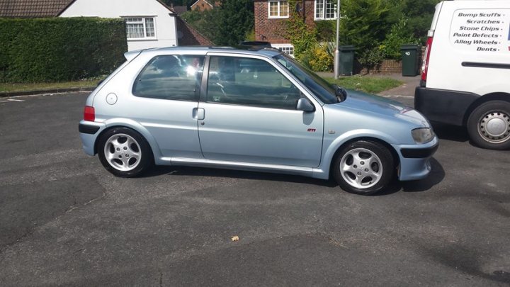 A white car parked next to a parking meter - Pistonheads - The image depicts a gray compact car parked in a driveway. The car has a small, two-door hatchback design, featuring a spoiler on the trunk. The driveway is situated in front of a home with a clearly visible lawn and shrubbery. In the background, there is a van parked behind the compact car.