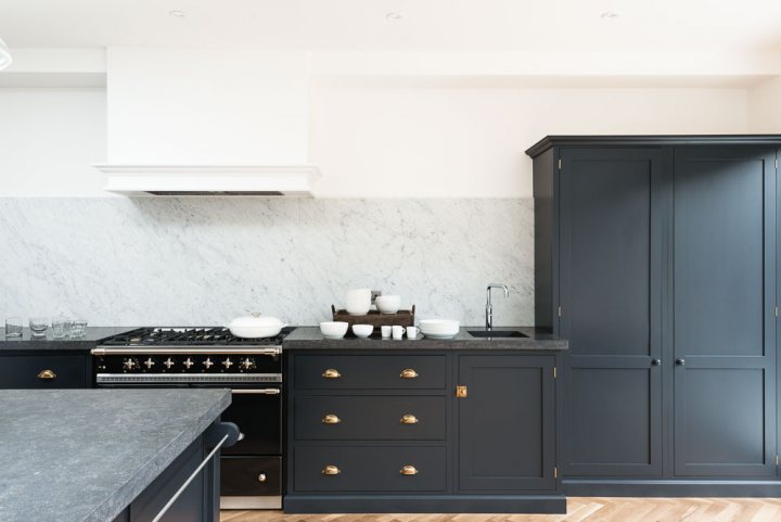 Kitchen plinth style? - Page 1 - Homes, Gardens and DIY - PistonHeads - The image presents a modern kitchen interior. A tall gray cabinet dominates the left side of the space, while a smaller white cabinet can be seen on the opposite side. The kitchen countertops are made of a dark material, providing a striking contrast to the lighter backsplash. On the counter, there are a few white bowls and some dishes, suggesting recent or upcoming use. The overall aesthetic of the kitchen is sleek and contemporary.