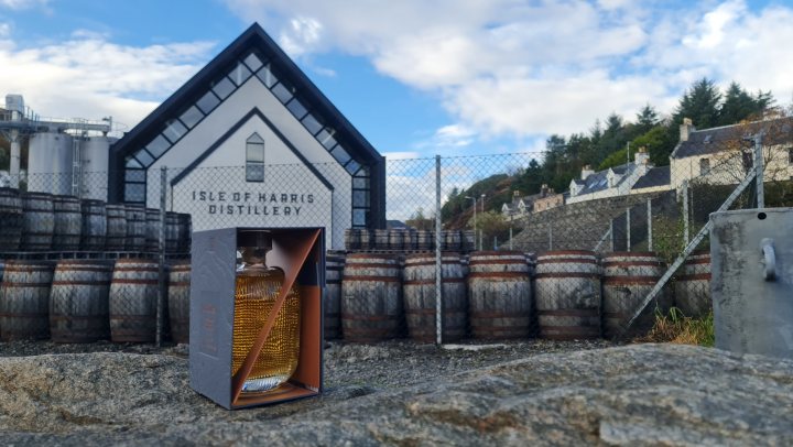 Show us your whisky! Vol 2 - Page 261 - Food, Drink & Restaurants - PistonHeads UK - The image captures a quaint scene of an outdoor distillery. A small building with a sign on the front stands as the focal point. Adjacent to this building, there are multiple wooden barrels stacked together, suggesting the process of aging and storing the distilled products. The barrels seem well-maintained and are quite prominent in the image.

In the background, a white house can be seen under a clear blue sky, adding a residential touch to the industrial feel of the distillery. The overall setting appears to be in a rural or semi-rural area, as indicated by the open space and natural lighting.