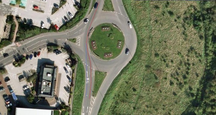 Ignoring Pistonheads Lane Markings - The image is an aerial, bird's-eye view of an urban area, featuring a complex web of roads intersecting and dividing the area. These roads are lined with a variety of vehicles in different lanes, suggesting a busy and bustling environment. There are also several patches of green space scattered throughout the area, likely parks or gardens, adding a touch of nature to the urban landscape. The buildings, roads, and vehicles all indicate a developed, densely populated cityscape.