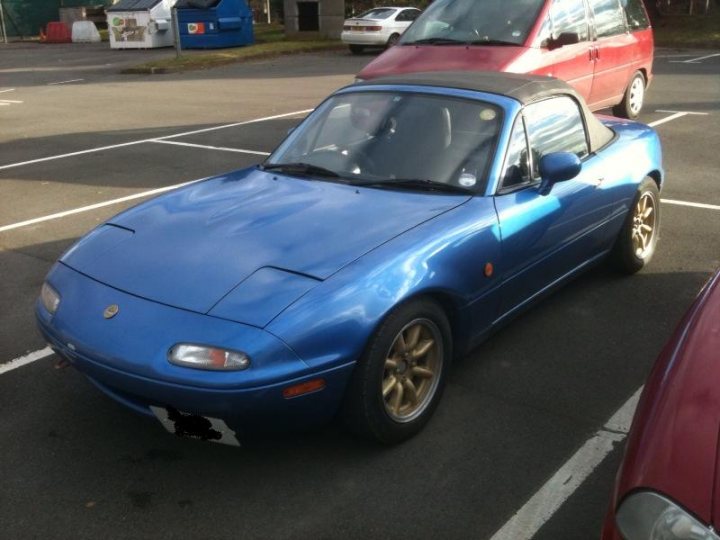 £3k, too steep? plus introduction - Page 1 - Mazda MX5/Eunos/Miata - PistonHeads - The image shows a vibrant blue sports car parked on the street. The car features a convertible top and a handicapped parking sticker on the window. Numerous other cars and vehicles, both parked and in motion, are visible in the background, adding a dynamic sense of urban life. The focus, however, remains on the elegant sports car.