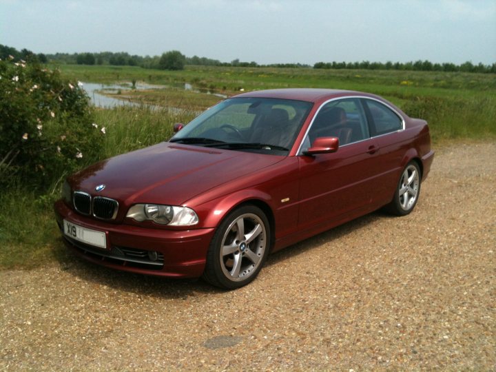 Stolen BMW 330Ci  X198 HDL SIENNA RED. - Page 1 - Kent & Essex - PistonHeads - The image features a red BMW parked on a gravel surface adjacent to a grassy area with trees. The car is a two-door coupe with a license plate that reads "TE 18." The surroundings suggest a countryside or rural environment. The vehicle has alloy wheels and the BMW emblem is visible on the hood and front fender.