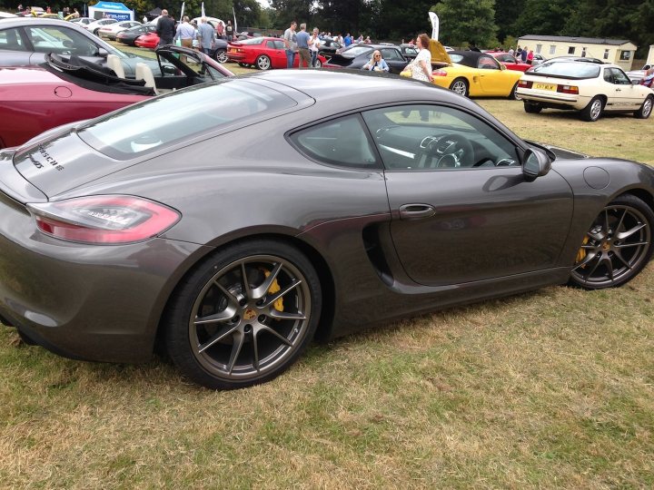 A car is parked in a parking lot - Pistonheads - This image captures a scene at a car show where various sports cars are on display. The central focus of the image is a black sports car positioned slightly to the left. The car show is bustling with people, some closer and others further away, scattered throughout the scene, observing and admiring the vehicles. The setting appears to be an open field with well-maintained grass. In the background, other cars can be seen, indicating the diversity of vehicles at the show. The atmosphere is lively, with the intricate details of the sports car on the left and the crowd, suggesting that the car show is a popular event.