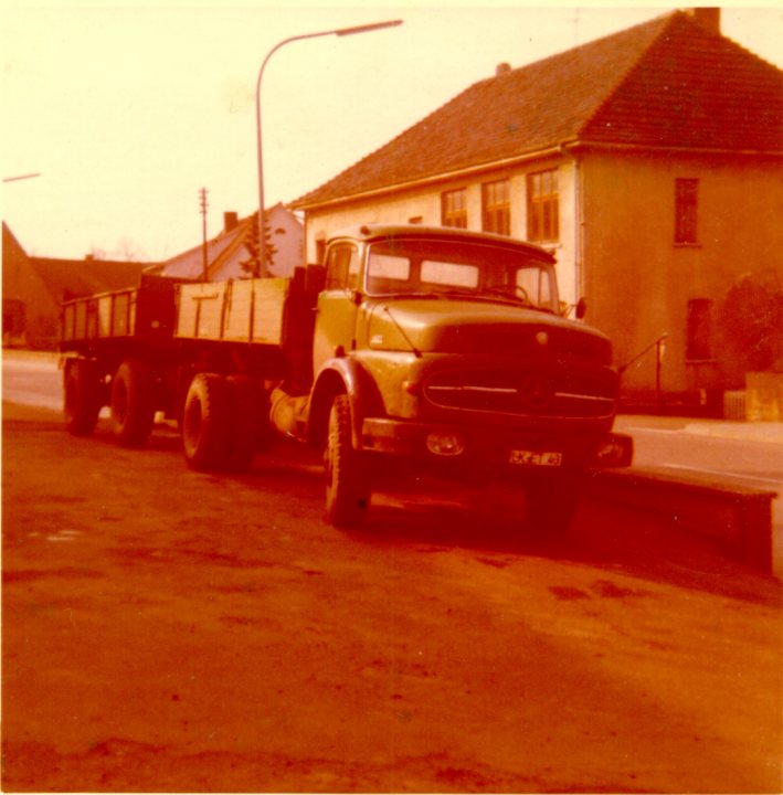 Pistonheads - The image shows a large green dump truck parked on a street. The truck spans a significant portion of the frame, with its cargo bed and front visible. Behind the truck, there is a single-story house with a pitched roof. To the left of the house, there is a street lamp partially obscured by the vehicle. The image has a golden tone, suggesting it might be from a time when colored film wasn't as sophisticated and might have been altered or taken under certain lighting conditions.