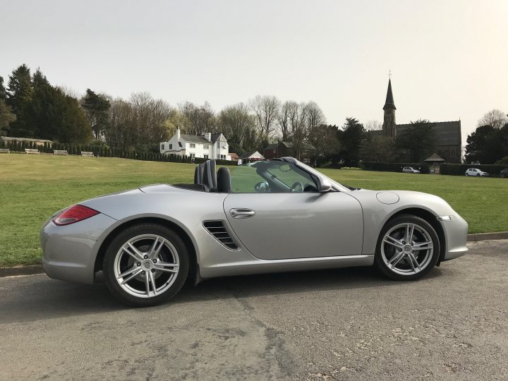 Who else is getting their Summer cars out?  - Page 7 - General Gassing - PistonHeads UK - The image shows a silver Porsche sports car parked outdoors. It's a convertible model with the top down, and it's equipped with large wheels that have a multi-spoke design. The car is positioned against a backdrop of green grass, trees, and a clear sky. In the background, there is a church spire and some buildings visible, suggesting the location might be a town or village. The image is a standard photograph with natural lighting, and it captures the vehicle from a three-quarter perspective, focusing on its front side profile.