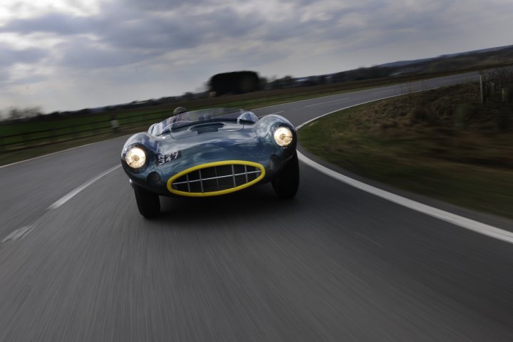 Aston Asm Replica Pistonheads Dbr Martin - This image captures a moment of a car speeding down a curvy road. The car appears to be a classic or vintage model, possibly a racing car, based on its aerodynamic design and distinctive front grille. The car is blurred in motion, suggesting high speed, along with the overcast sky in the upper background, which adds a dramatic effect and motion to the image. The road curves gently left and descends slightly, implying a sense of depth and a journey through the landscape.