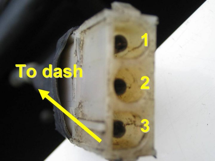 Electronic Box Pistonheads Identification - The image displays a close-up of a mechanical component, which appears to be an engine part as indicated by the text "TO DASH". The component is primarily white and features three black circles arranged in a line. The photograph's focus is on the top left black circle of this device, highlighting this specific detail with a yellow arrow pointing to it. The background of the image is darker, providing contrast that accentuates the component.